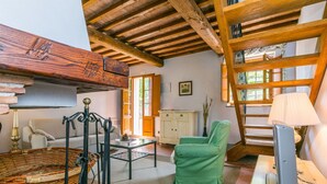 Une pièce rustique avec des poutres apparentes, un panier en osier, une chaise verte, une armoire blanche et une échelle.