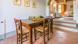 Un coin repas avec une table et des chaises en bois, un panier de fruits et, au mur, des reproductions encadrées de gravures botaniques.