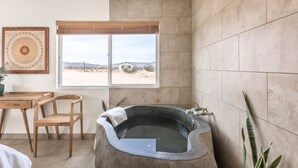 Un bagno moderno con una grande vasca da bagno, un tavolo in legno con sedie e vista sul deserto attraverso un'ampia finestra.