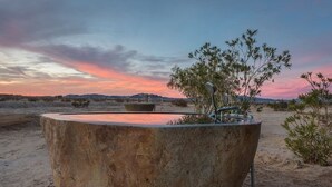 Un'imponente struttura in cemento con un elemento d'acqua, circondata da vegetazione rada e un paesaggio desertico.