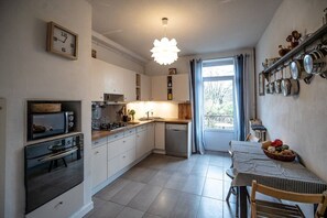 A compact kitchen with a microwave, stove, and dishwasher, a dining table with chairs, and a window with curtains.