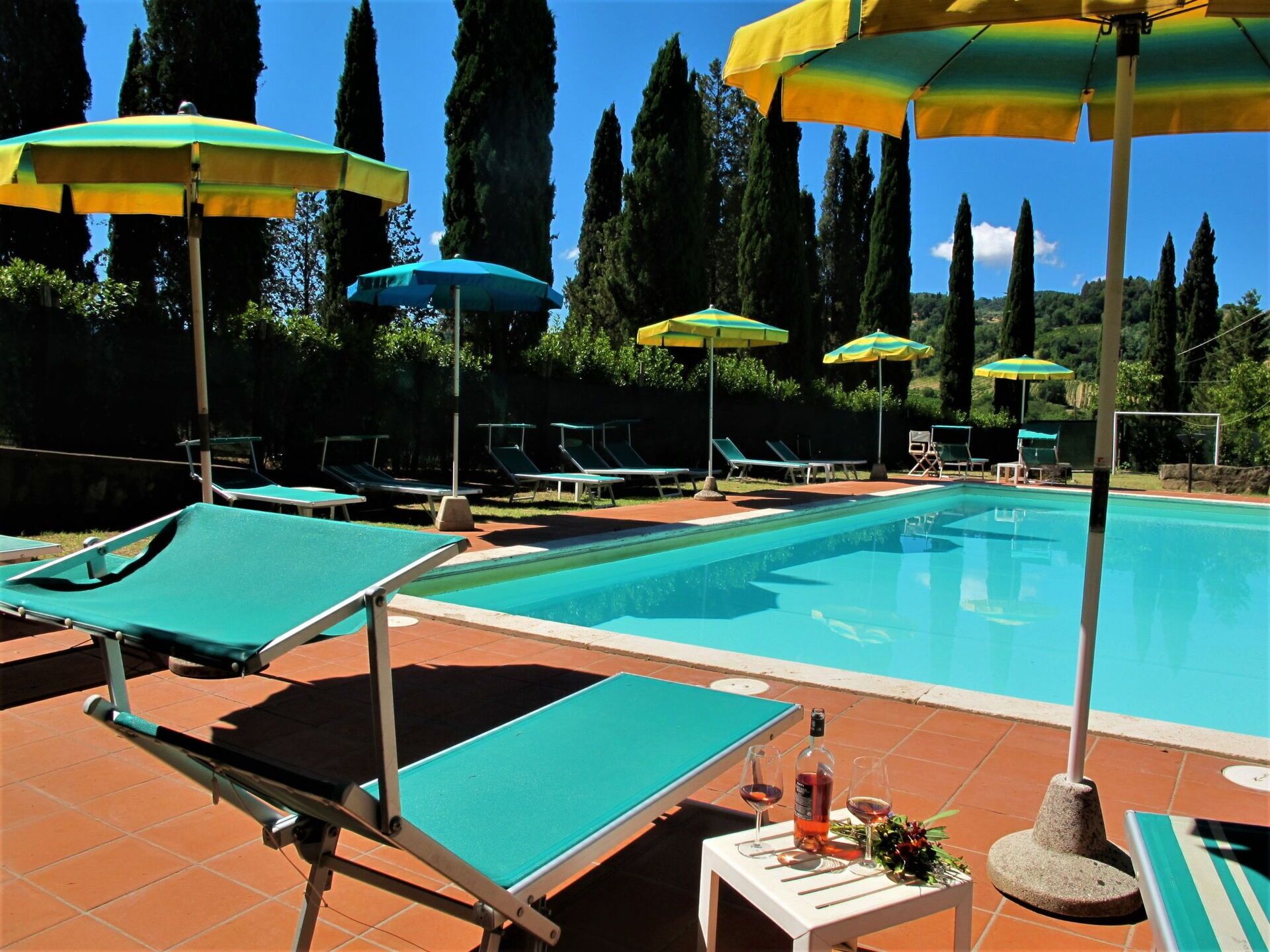 A swimming pool with lounge chairs and umbrellas, surrounded by tall trees.