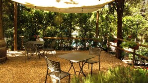Um pátio externo com mesa e cadeiras, cercado por árvores e um cercado de madeira.