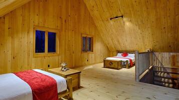 A wooden cabin with two bedrooms, each with a bed and a window. There is a small table with a teddy bear in the first room.