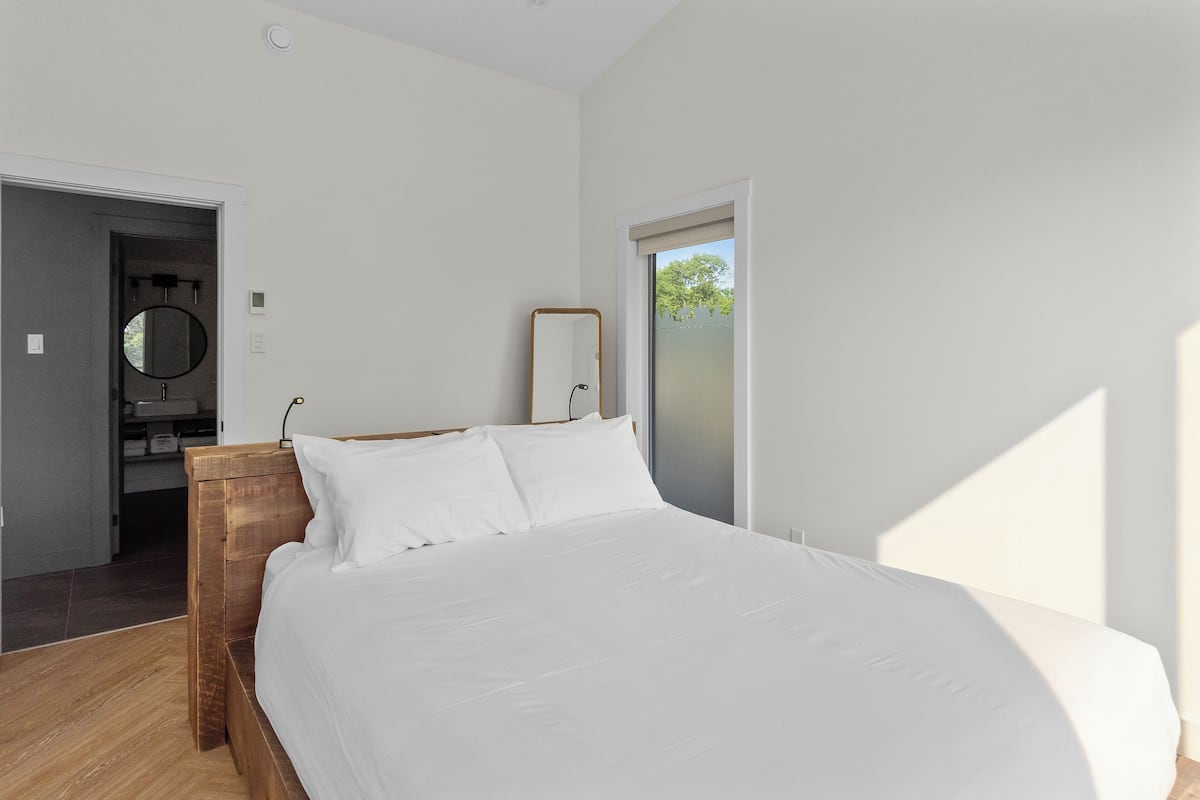 Un dormitorio con una cama grande, una mesita de noche de madera, un espejo y una puerta que da al baño.