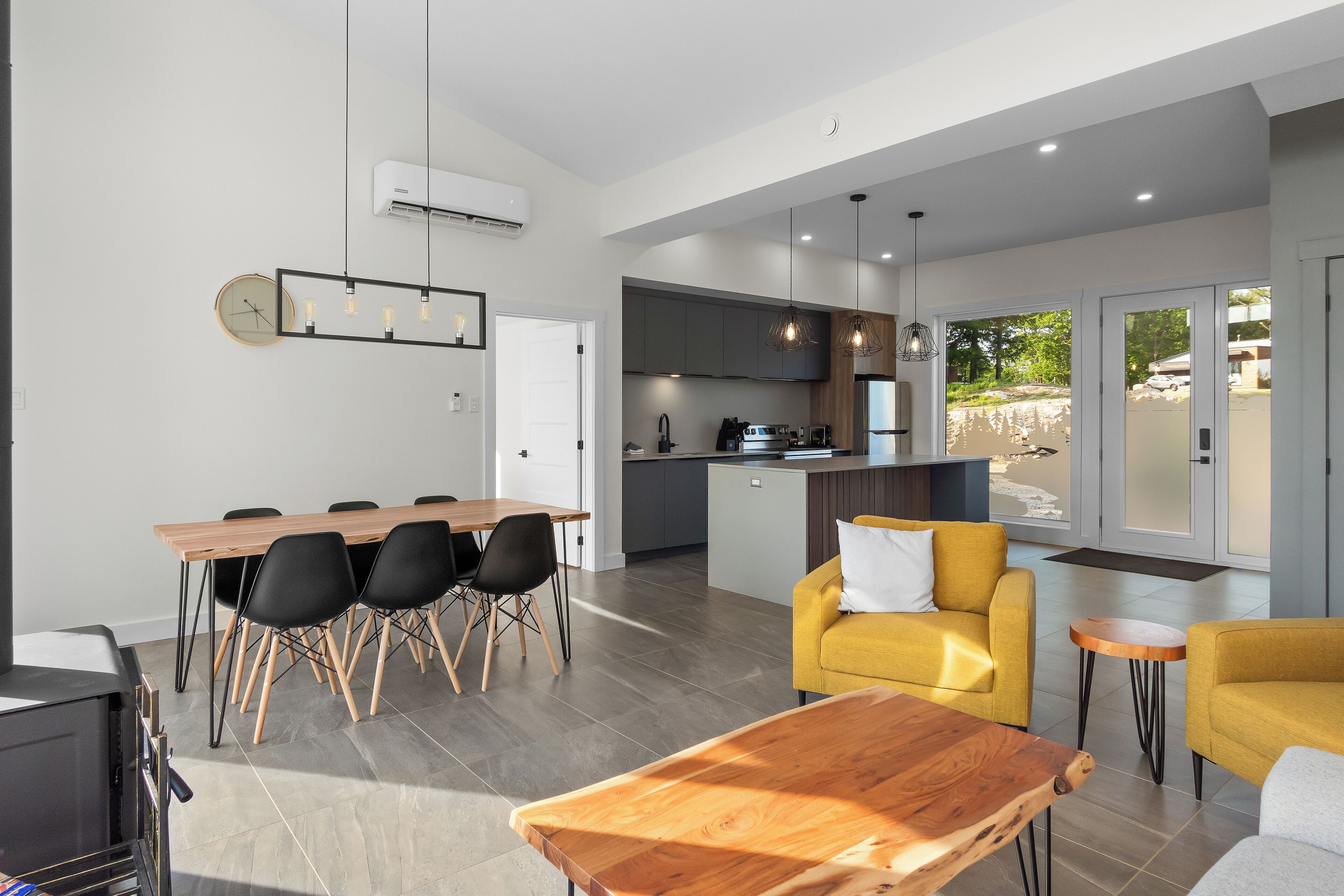 A modern kitchen with dark cabinets, a central island, and a dining area with a wooden table and chairs.