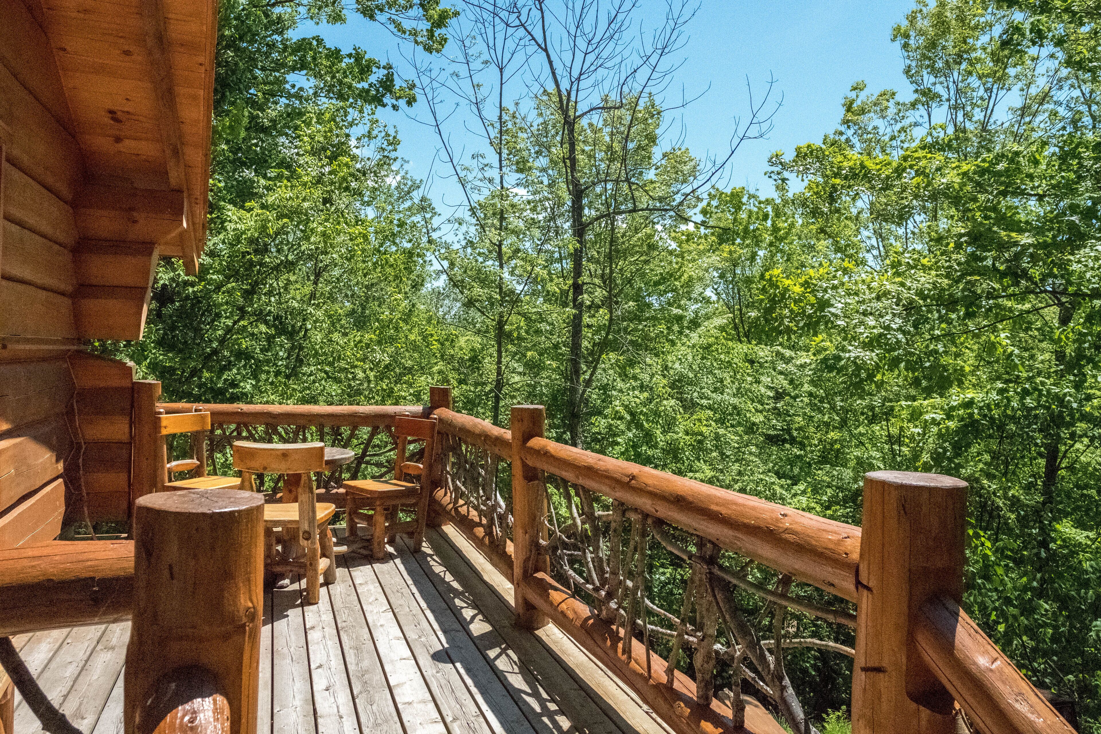 Una terraza de madera con mobiliario exterior y barandilla, con vistas a un área boscosa.
