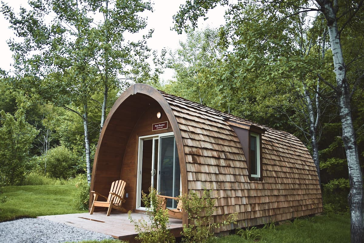 Una cabaña de madera con techo inclinado, un porche con una silla y un letrero que dice "Pod Erale".