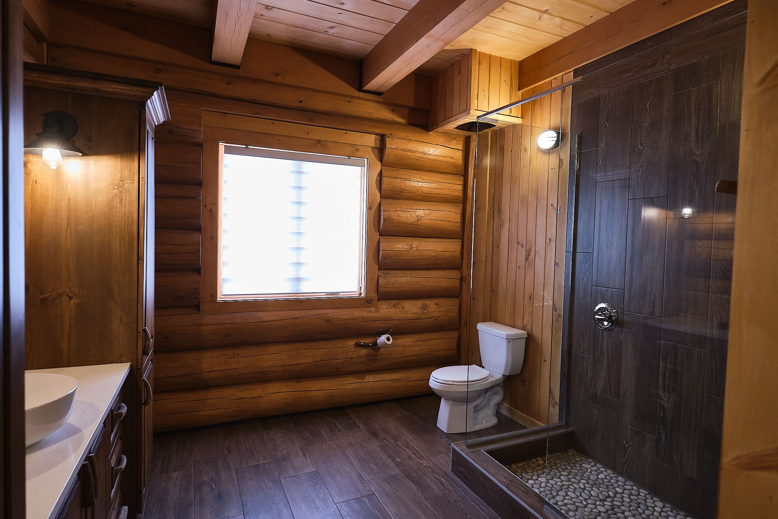 Ein Badezimmer einer Holzhütte mit Toilette, Waschbecken und Dusche.
