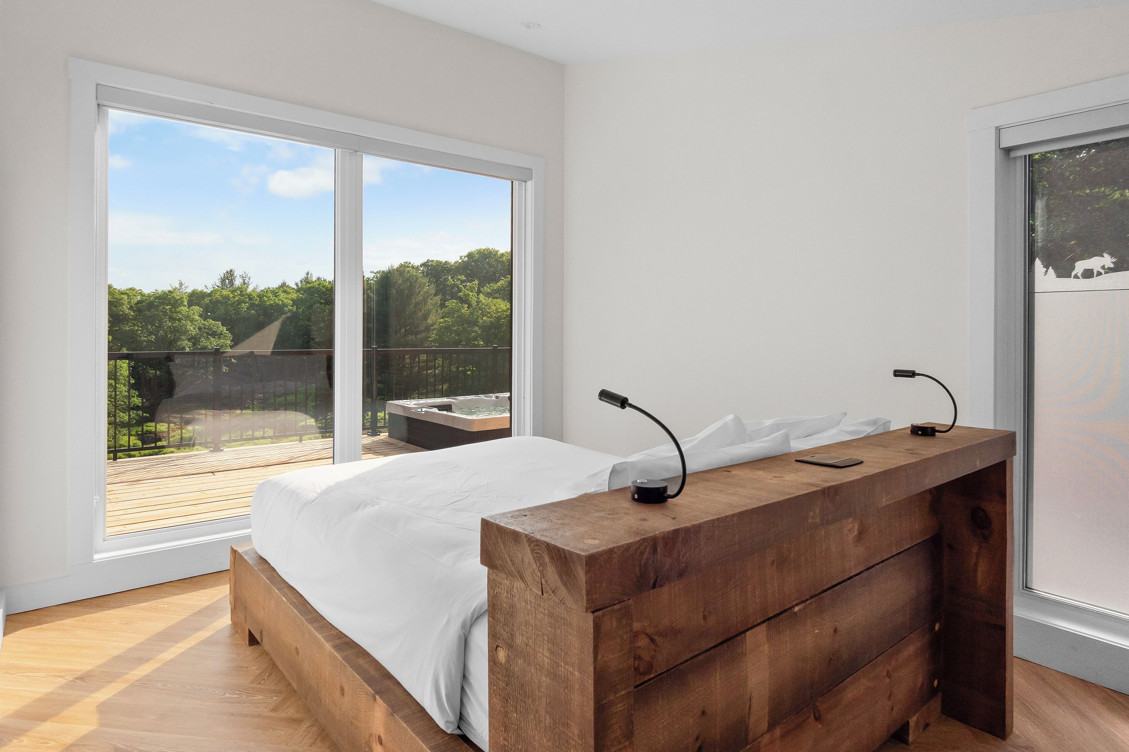 Un dormitorio con estructura de cama de madera, mesita de noche de madera y un gran ventanal corredero que da a una terraza exterior.