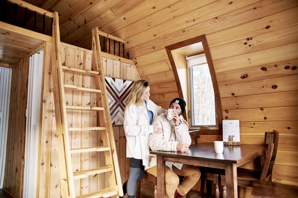 Un interior de madera con una cama en literas, una mesa de comedor y una ventana.