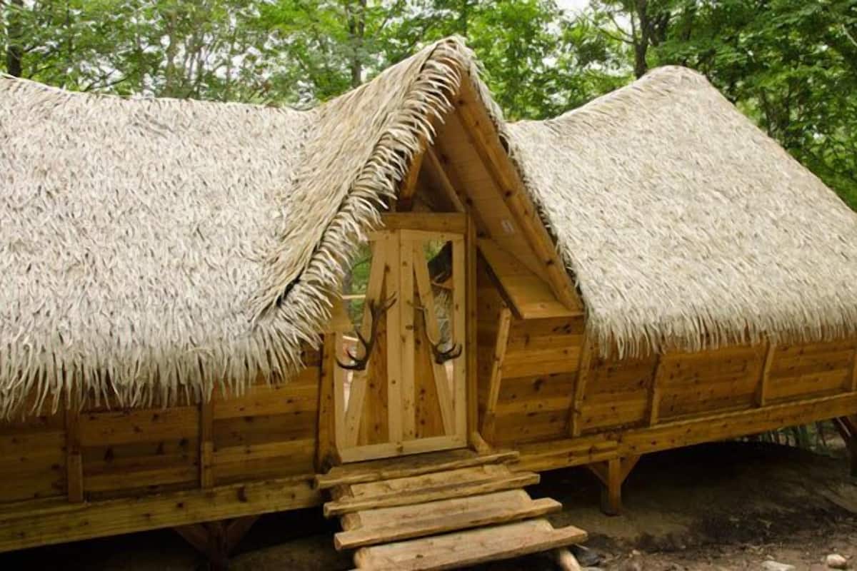 Una cabaña de madera con techo de paja, una puerta de madera y un conjunto de escalones de madera que conducen a la entrada.
