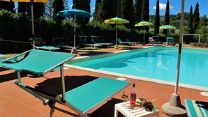 Una piscina con lettini e ombrelloni, circondata da alberi alti.