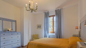 Una camera da letto con un letto, una cassettiera, una sedia, una finestra con tende e un lampadario.