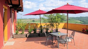 Una terrazza con tavolo e sedie, ombrelloni rossi e piante in vaso.