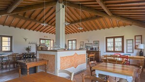 Un'ampia sala da pranzo con tavoli e sedie in legno, un'isola centrale con sgabelli da bar e un alto soffitto in legno con travi a vista.