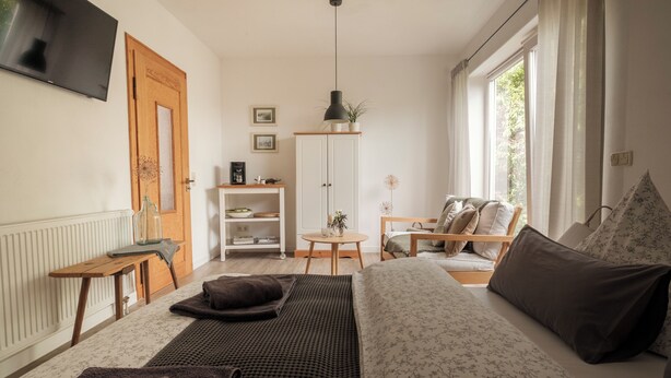 A cozy living room with a sofa, a coffee table, a TV, and a window with curtains. - Vacation apartment CramerTwo rooms for 4 persons (Gerolzhofen)