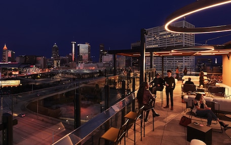 A rooftop bar with a city view, seating, and a glass railing overlooking the streets.