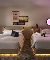 Quarto de hotel com duas camas, piso coberto por carpete e obras de arte na parede.