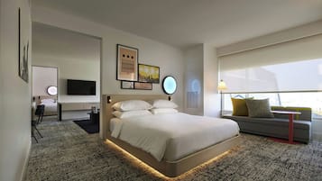A modern hotel room with a large bed, a sofa, a TV, and artwork on the walls.
