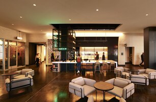 A modern hotel lobby with seating areas, a check-in counter, and a bar.