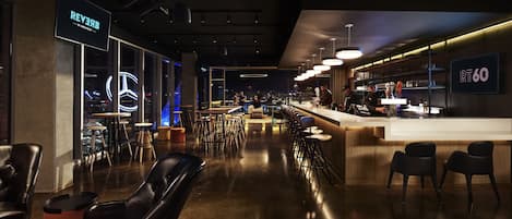 Zona de bar moderna con taburetes altos, barra y vistas a la ciudad a través de amplios ventanales.