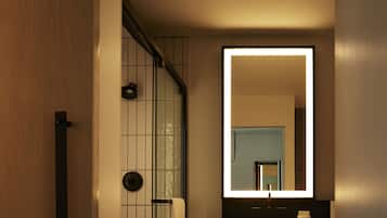 Un bagno moderno con porta in legno, cabina doccia in vetro, uno specchio grande e lavabo integrato.