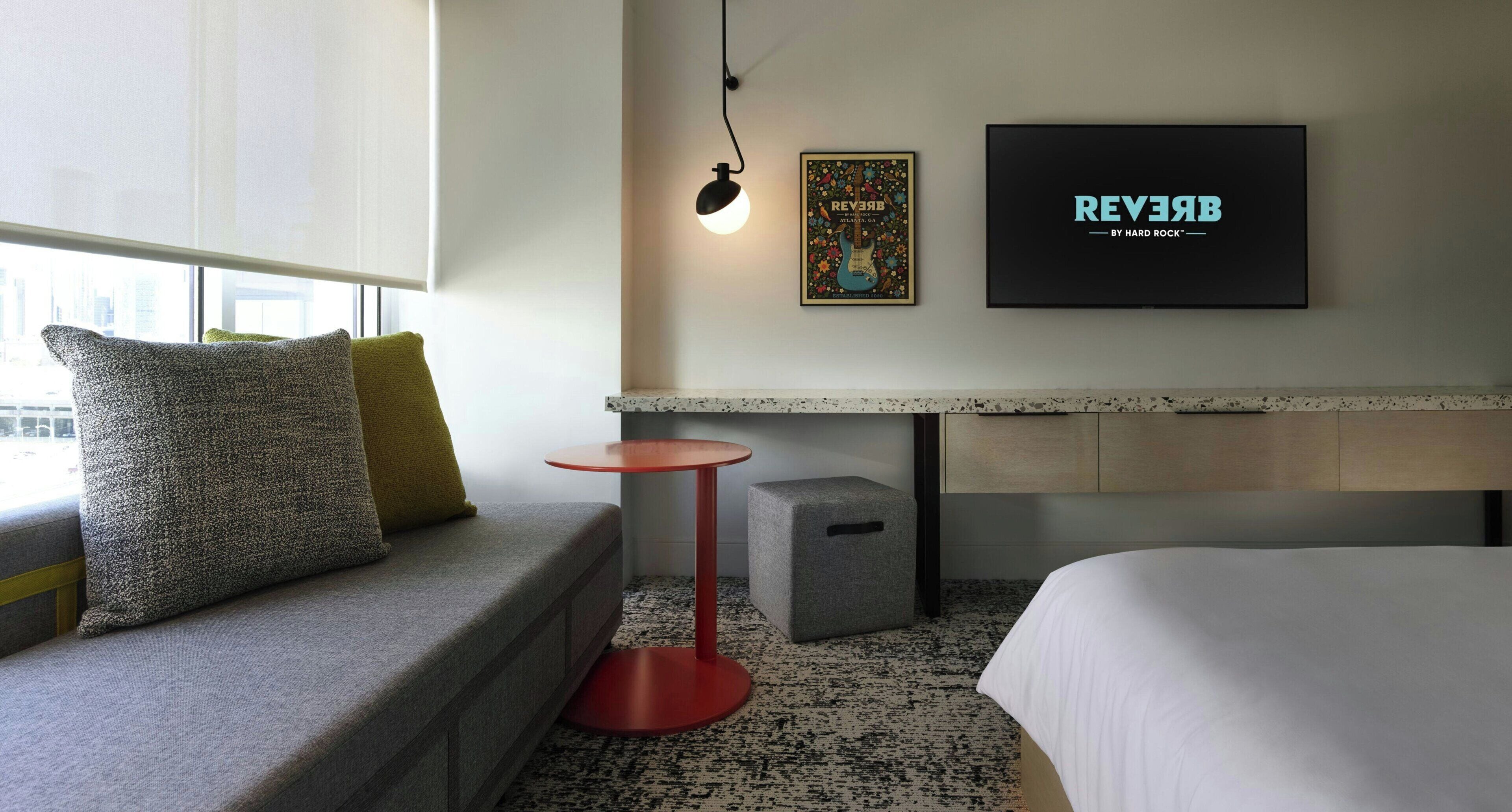 Une chambre d’hôtel avec un lit, une petite table ronde, un canapé avec des coussins, une lampe fixée au mur et deux tableaux encadrés.