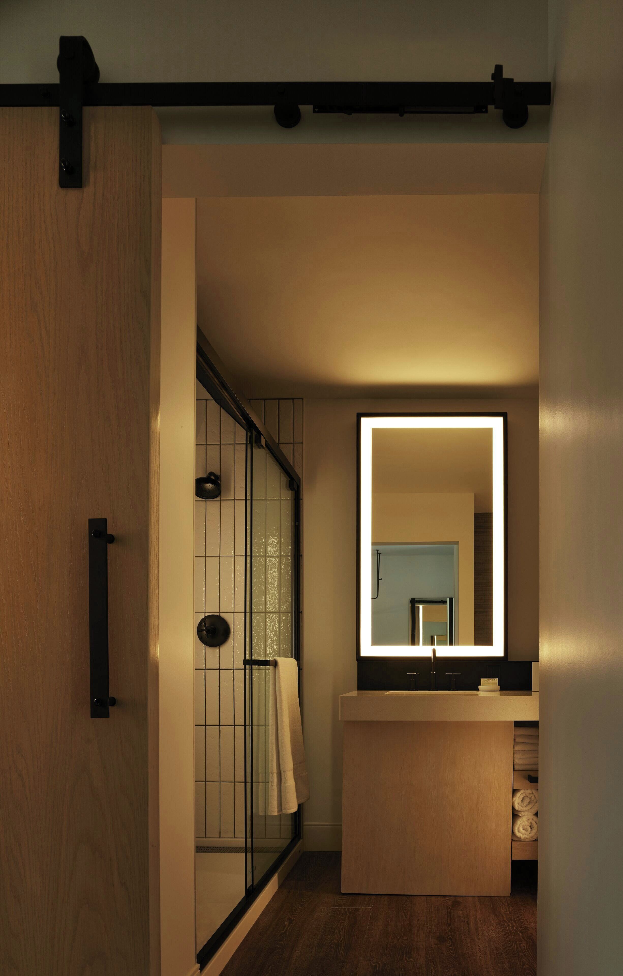 Un baño moderno con suelo de madera, cabina de ducha de vidrio, un espejo grande y un mueble de tocador de madera.