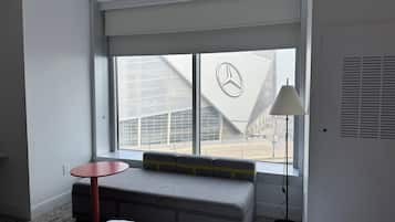 A hotel room with a large window, a bench, a small table, and a lamp.