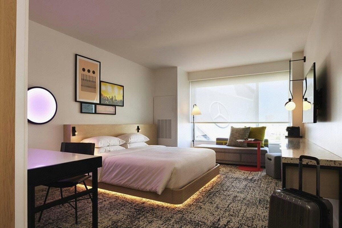 A modern hotel room with a bed, bedside table, lamp, and a large window with a view.