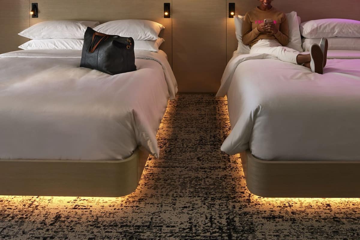A hotel room with two beds, a headboard with built-in lighting, a rug, and artwork on the wall.