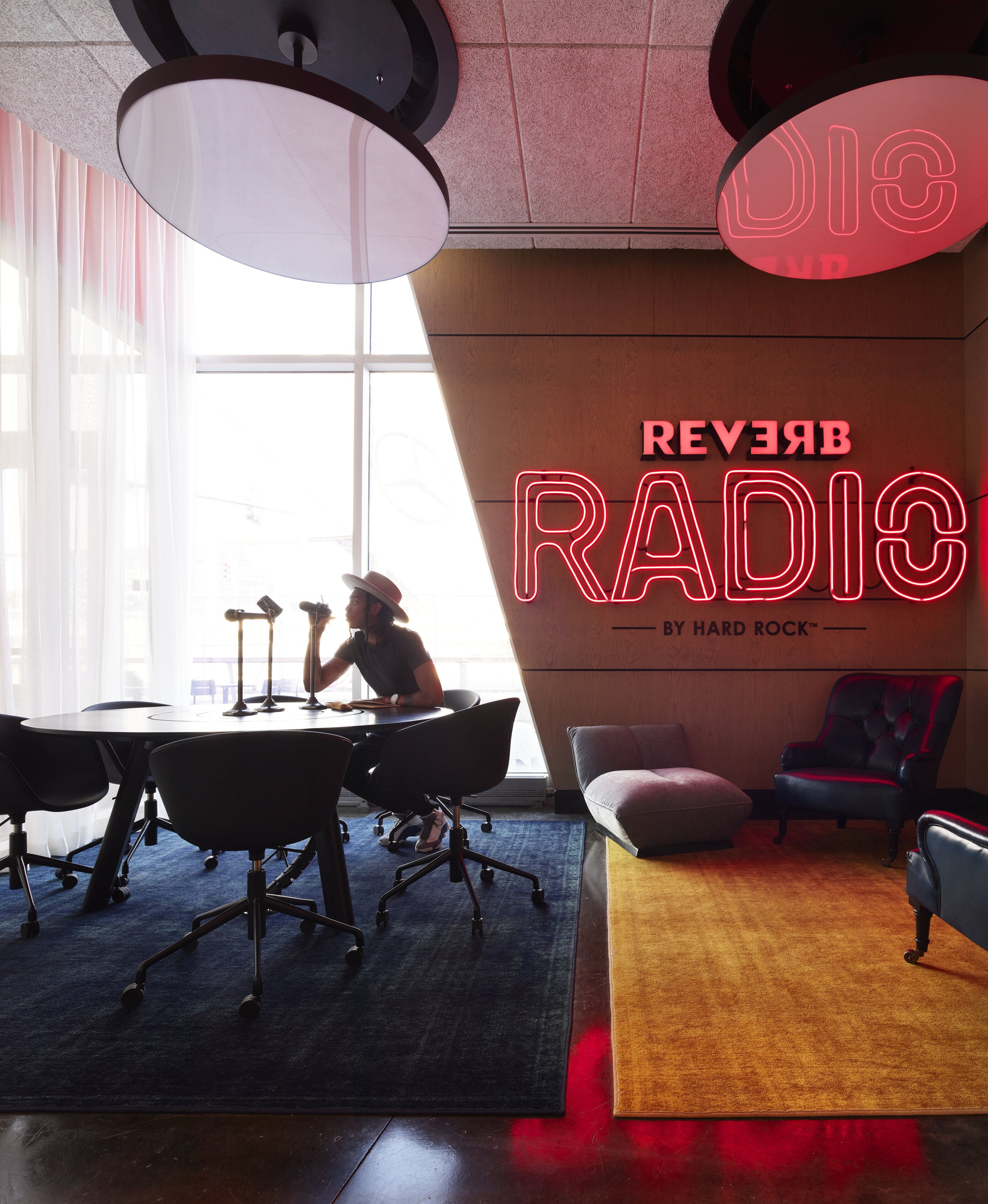 Un estudio de grabación con un letrero de neón que dice "REVERSERADIO" y una persona trabajando en un escritorio con equipo musical.