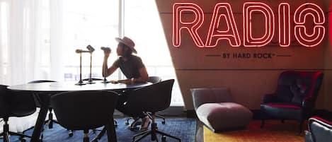 Un estudio de grabación con un letrero de neón que dice "REVERSERADIO" y una persona trabajando en un escritorio con equipo musical.