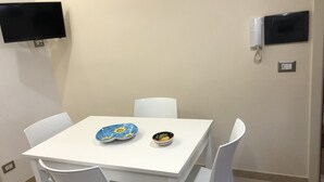 Pieni ruokailutila, jossa on valkoinen pöytä ja neljä valkoista tuolia. Pöydällä on kaksi koristeellista lautasesta.