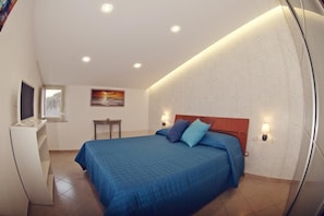 Un dormitorio con una cama grande, un televisor sobre un mueble bajo, una mesita y un cuadro en la pared.