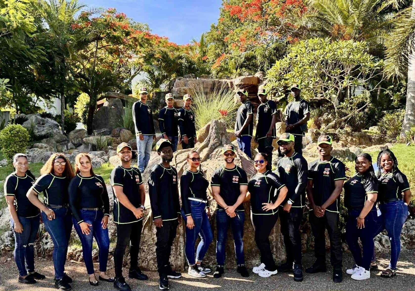 Een groep mensen in zwarte en groene uniformen staat buiten, met een natuurlijke achtergrond van bomen en rotsen.