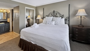 A neatly made bed with a white and gray striped pillow, a bedside lamp, and a dark wooden dresser in a hotel room.