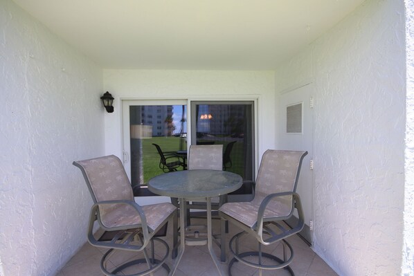 A small balcony with a glass door leading to a patio area. There are two metal chairs and a round table.