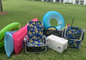 A grassy area with a pool float, a beach chair, a cooler, and a small portable table.