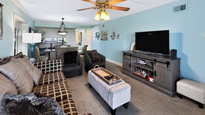 A living room with a sofa, ottoman, TV stand, and ceiling fan. - El Matador 111 -  FREE TICKETS!! Your stay includes free tickets to many area attractions! (Fort Walton Beach)