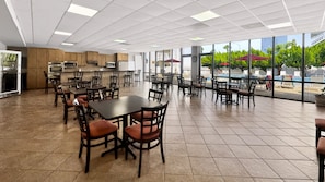 A spacious indoor dining area with multiple tables and chairs, a kitchen area with modern appliances, and large windows offering views of an outdoor pool area.