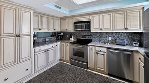 A modern kitchen with light-colored cabinetry, a black tiled backsplash, stainless steel appliances, and a skylight.