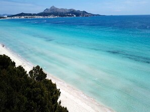 Une plage à l’eau turquoise et limpide, bordée d’un rivage sablonneux, avec une chaîne de montagnes en toile de fond.