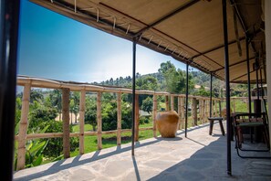 A covered terrace with stone flooring, a large pot, and a view of a lush landscape.