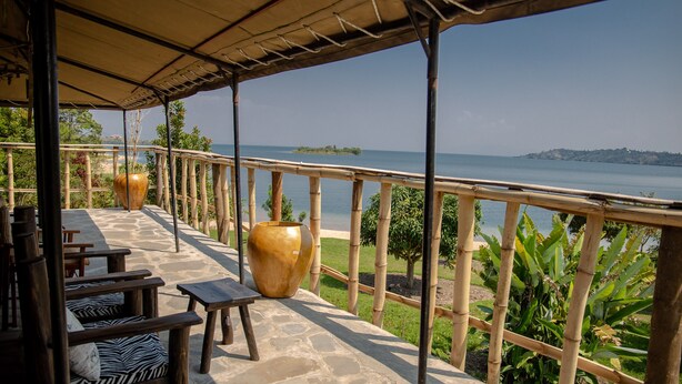 A covered outdoor seating area with stone flooring, wooden furniture, and large vases. - Rushel Kivu Lodge (Boneza)