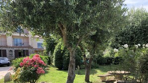 Ein Garten mit einer Steinsitzbank, einem großen Felsen und einem Auto vor einem Gebäude mit Balkonen.
