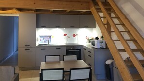 Eine kleine Küche mit grauen Schränken, einer Holztreppe und einem Essbereich mit zwei Stühlen.