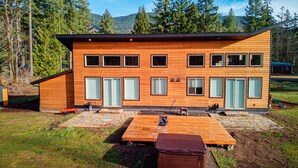 A modern wooden cabin with multiple windows, a stone patio, and a wooden deck. - Modern Chalet Duplex - 2 (Mount Hood Village)