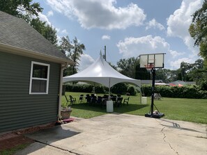 A backyard with a basketball hoop, a tent, and a house.